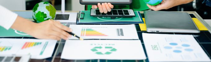 People evaluating papers and charts on a table while holding a laptop